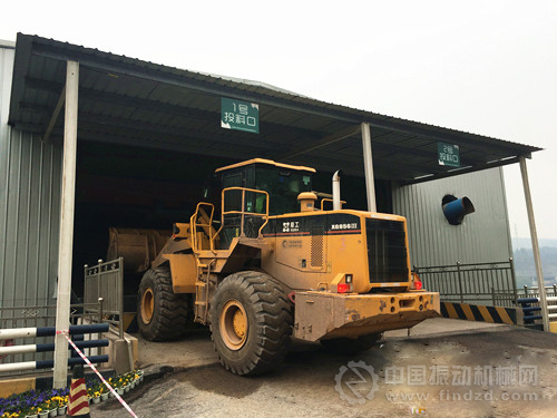 挖掘機正將建筑廢料投放到投料口。